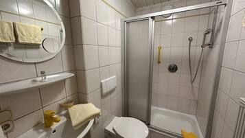 A bathroom with a toilet, sink, mirror, and shower.