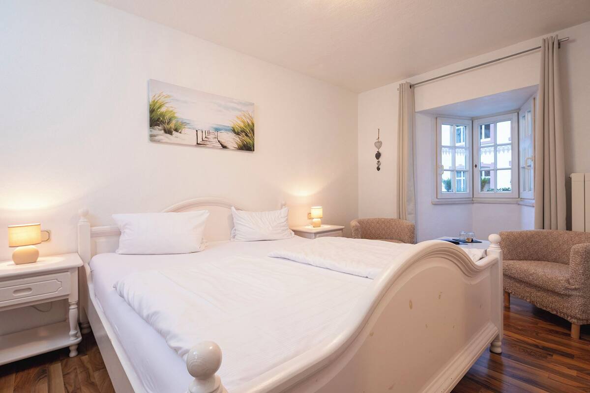 A bedroom with a large bed, two bedside tables with lamps, a chair, and a painting on the wall.