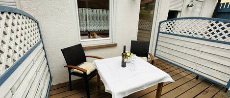 Un patio al aire libre con una mesa para dos, sillas y una botella de vino.