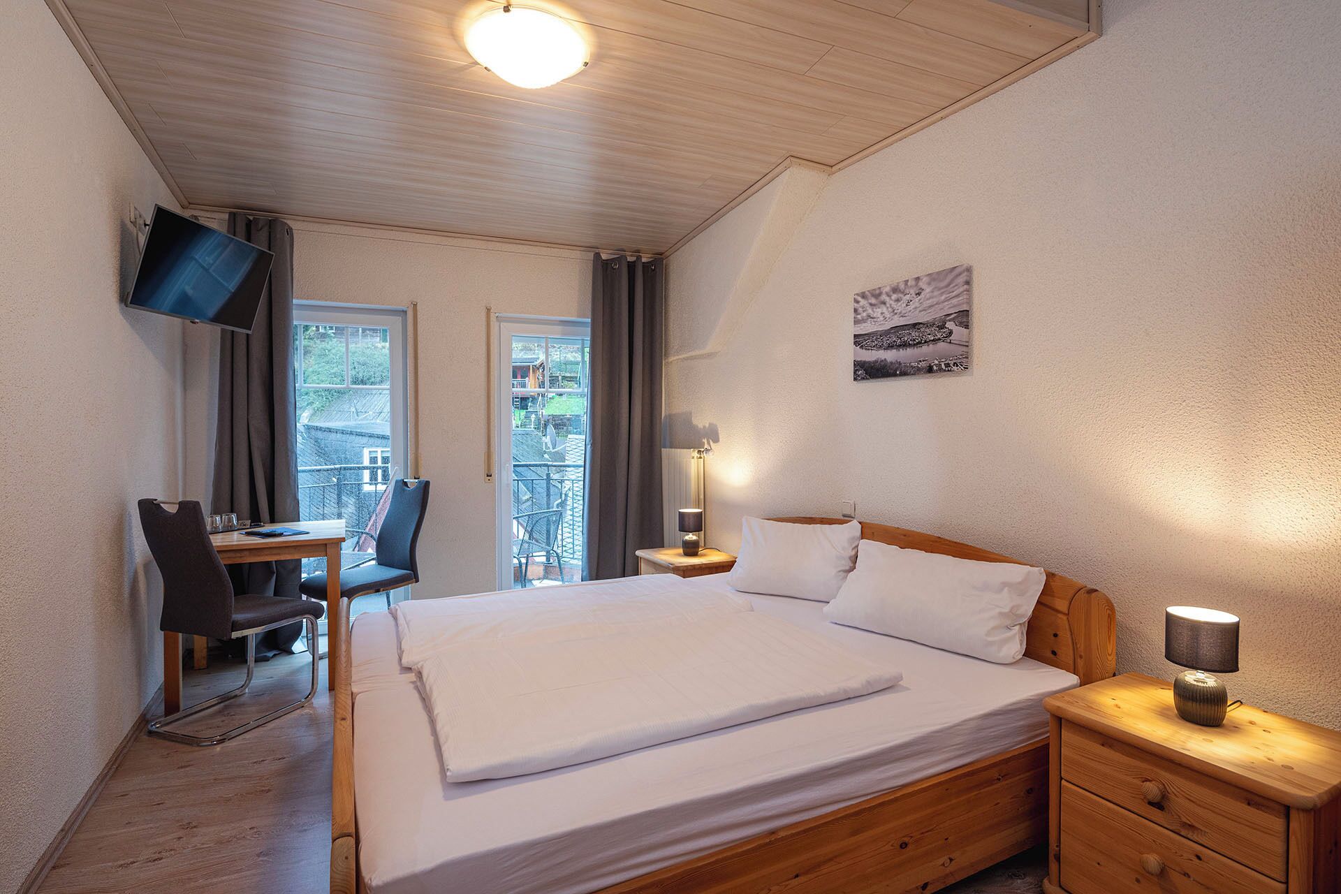 A hotel room with a bed, bedside table, lamp, TV mounted on the wall, and a balcony with a view.