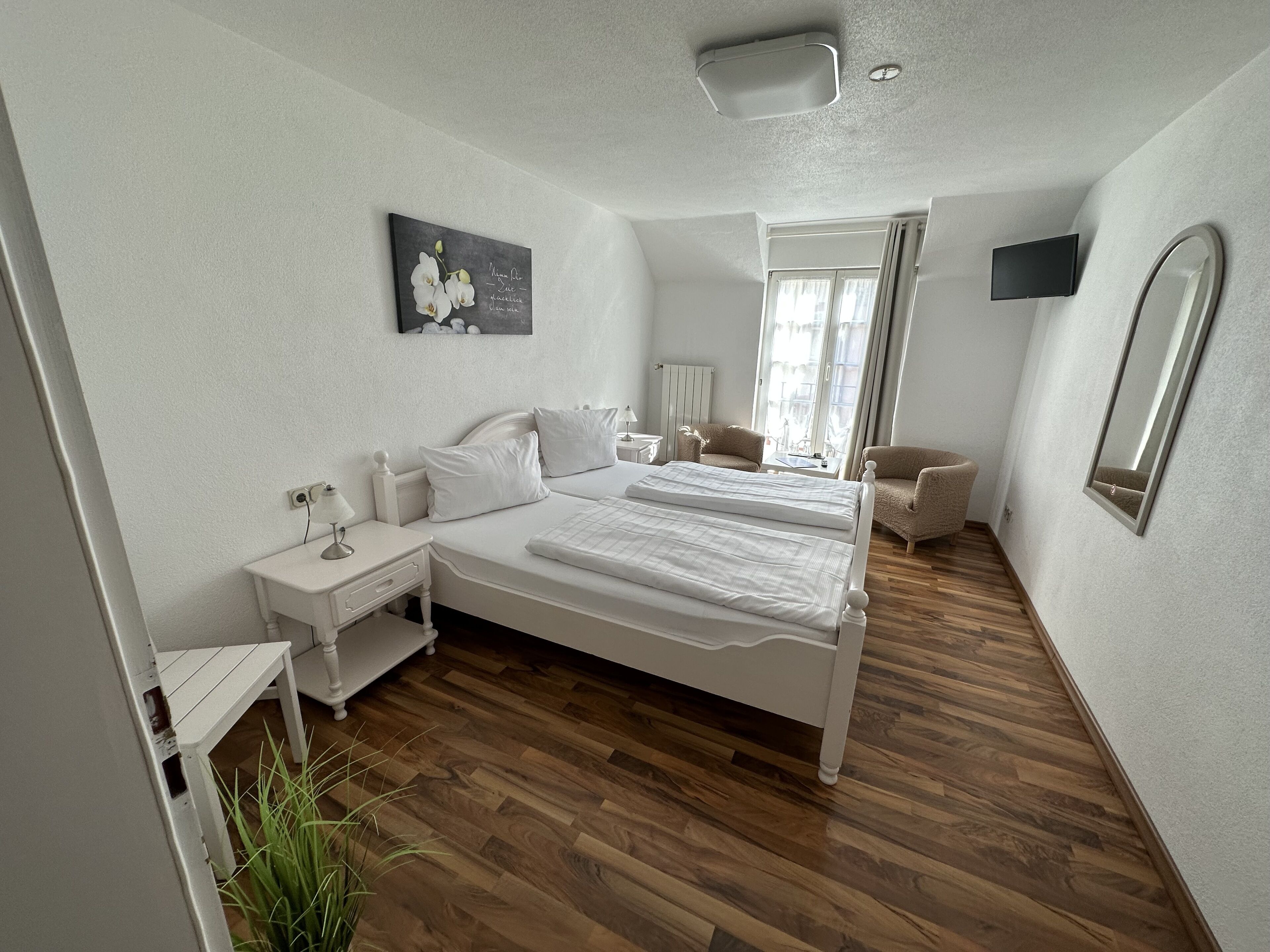 A bedroom with a double bed, bedside tables, a chair, a TV, and a painting on the wall.
