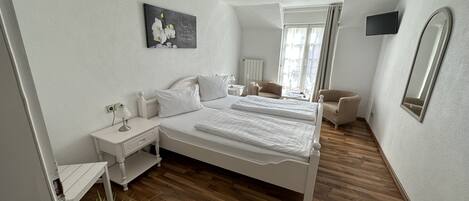 Une chambre à coucher avec un lit double, des tables de chevet, une chaise, un téléviseur et un tableau au mur.