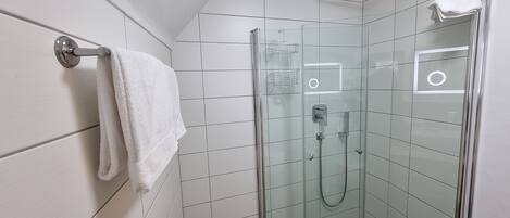 A modern shower with a glass enclosure, a white towel on a metal towel rack, and a tiled wall.