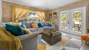 A cozy living room with a sectional sofa, a coffee table, and a view of the outdoors through a sliding glass door.