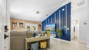 A modern living room with a sofa, coffee table, and TV. There is a blue accent wall with vertical lines and a wooden ceiling.