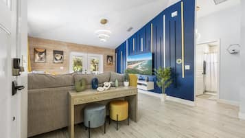 Un salon moderne avec un canapé, une table basse et un téléviseur. Un mur d’accent bleu, orné de lignes verticales, et un plafond en bois complètent l’ensemble.