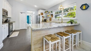A modern kitchen with white cabinetry, a marble countertop, and a central island with bar stools.