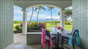 A covered patio with a view of the ocean, a table with chairs, and a number sign on the wall. - Beautiful ground floor unit right on the beach! (Lahaina)