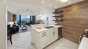A modern kitchen with a central island, a dining area with a view, and a living room with a large window. - Beautiful ground floor unit right on the beach! (Lahaina)