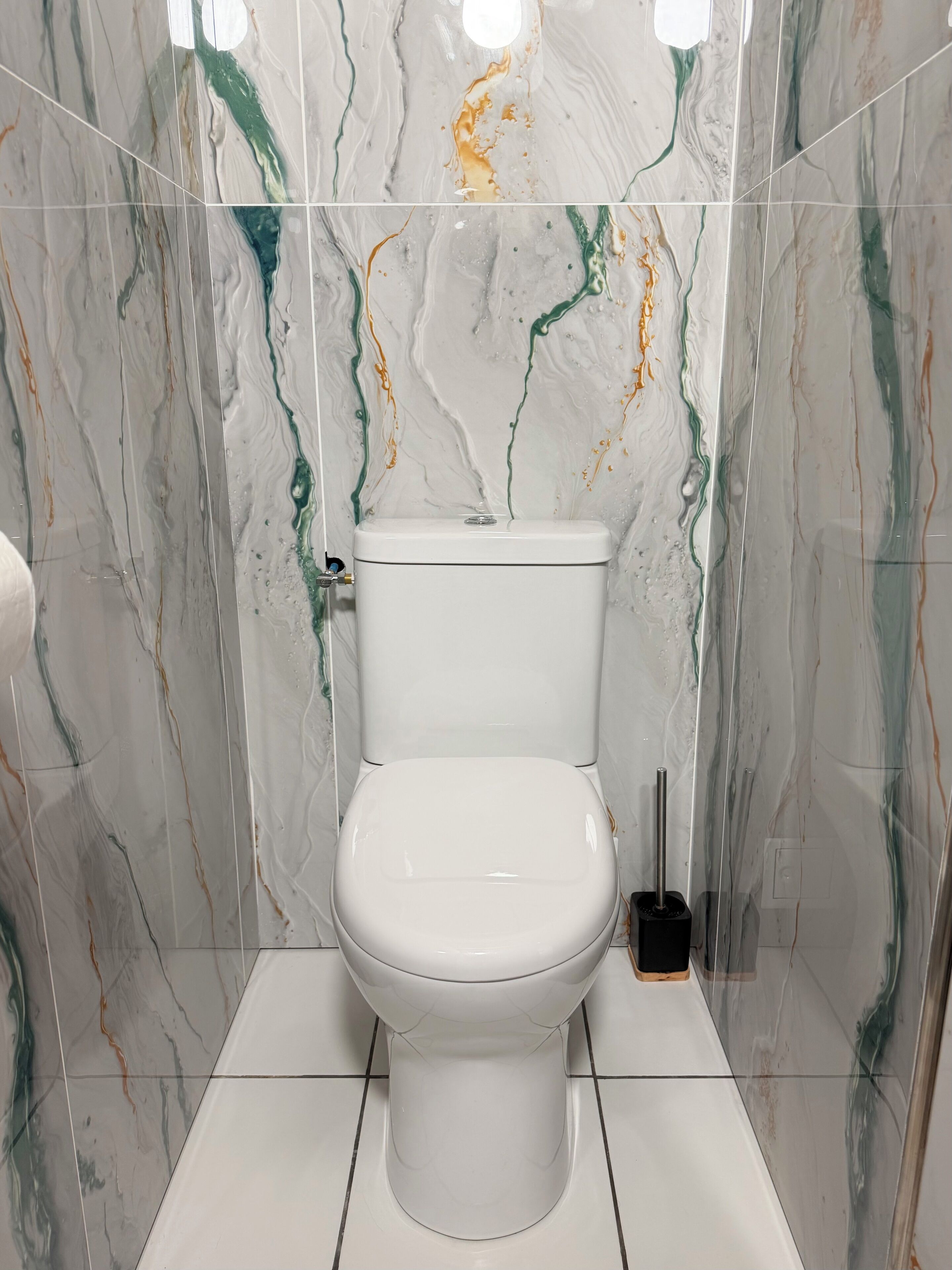 Une salle de bain avec des toilettes blanches, des murs à motifs de marbre et une brosse pour les toilettes.