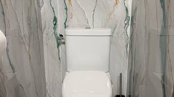 Une salle de bain avec des toilettes blanches, des murs à motifs de marbre et une brosse pour les toilettes.