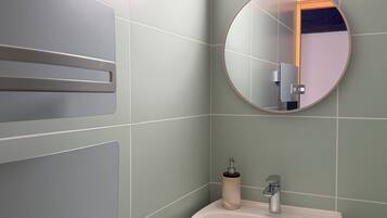 Un baño con un lavamanos blanco, un espejo redondo y una lámpara sobre el espejo.