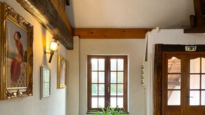 Un couloir avec une grande plante en pot, des poutres en bois et une porte sur laquelle est apposée une pancarte.