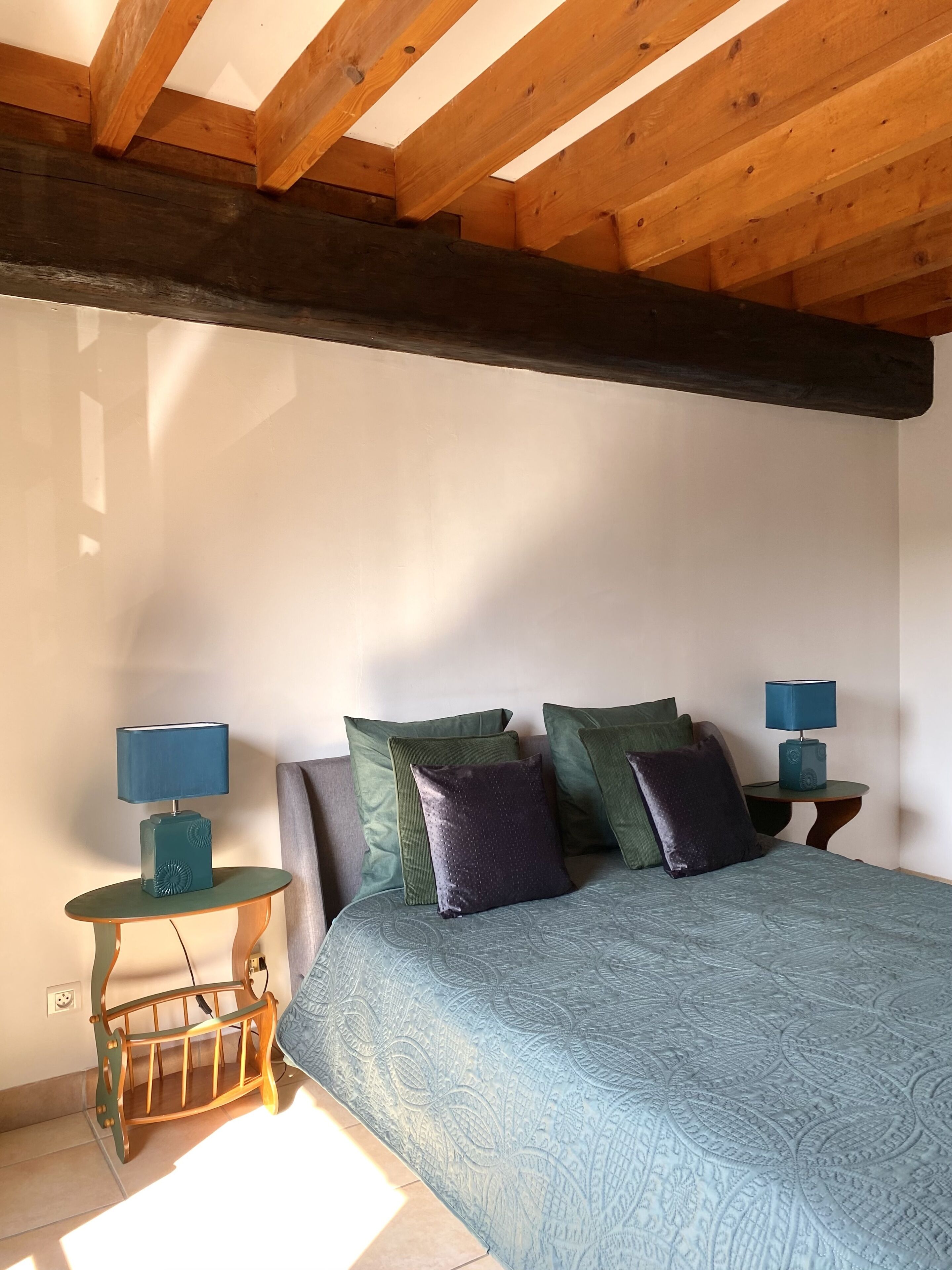 Une chambre avec un plafond en bois, un lit recouvert d’une couvre-lit à motifs et deux tables de chevet avec des lampes.