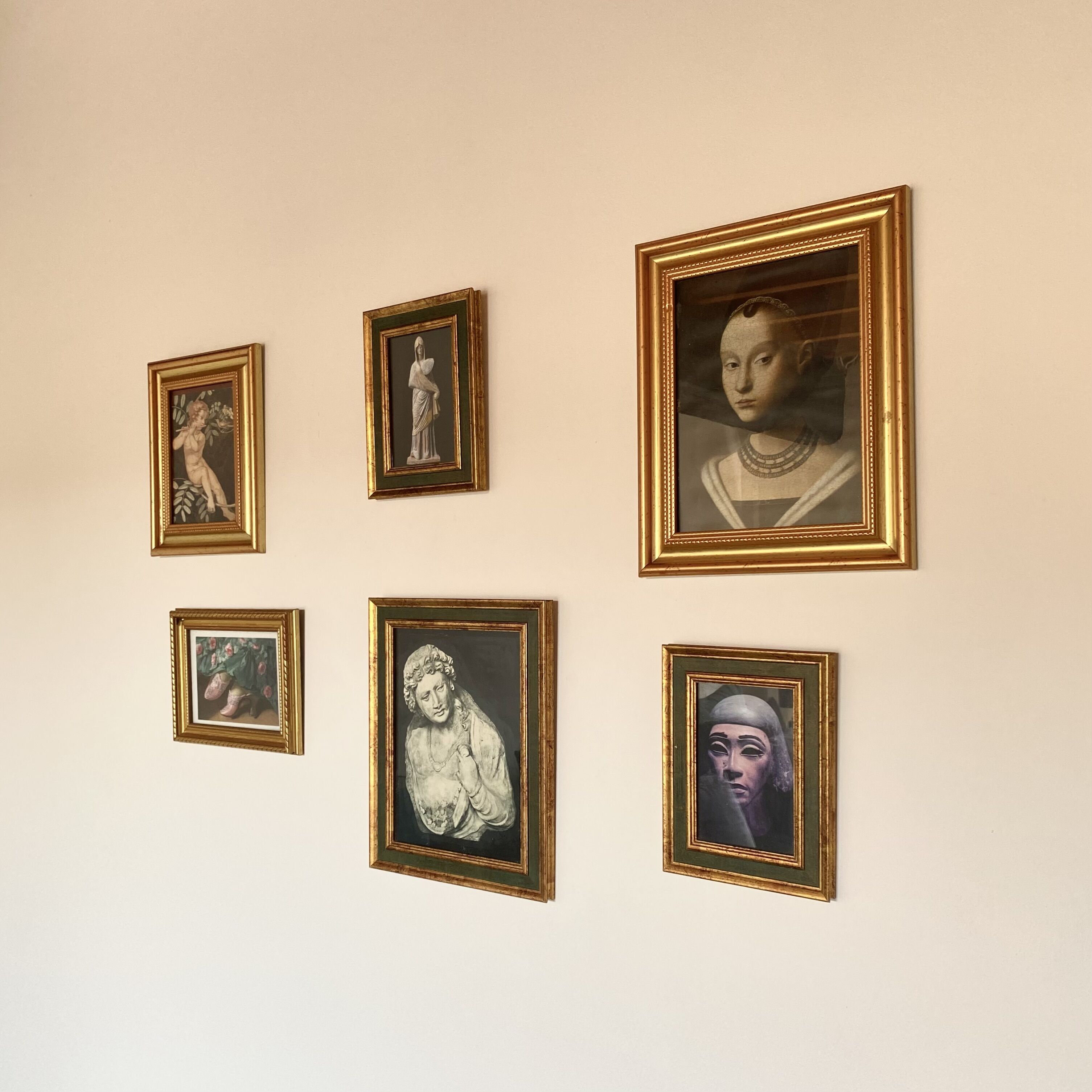 Uma parede com cinco obras de arte emolduradas, de tamanhos e temas diferentes.