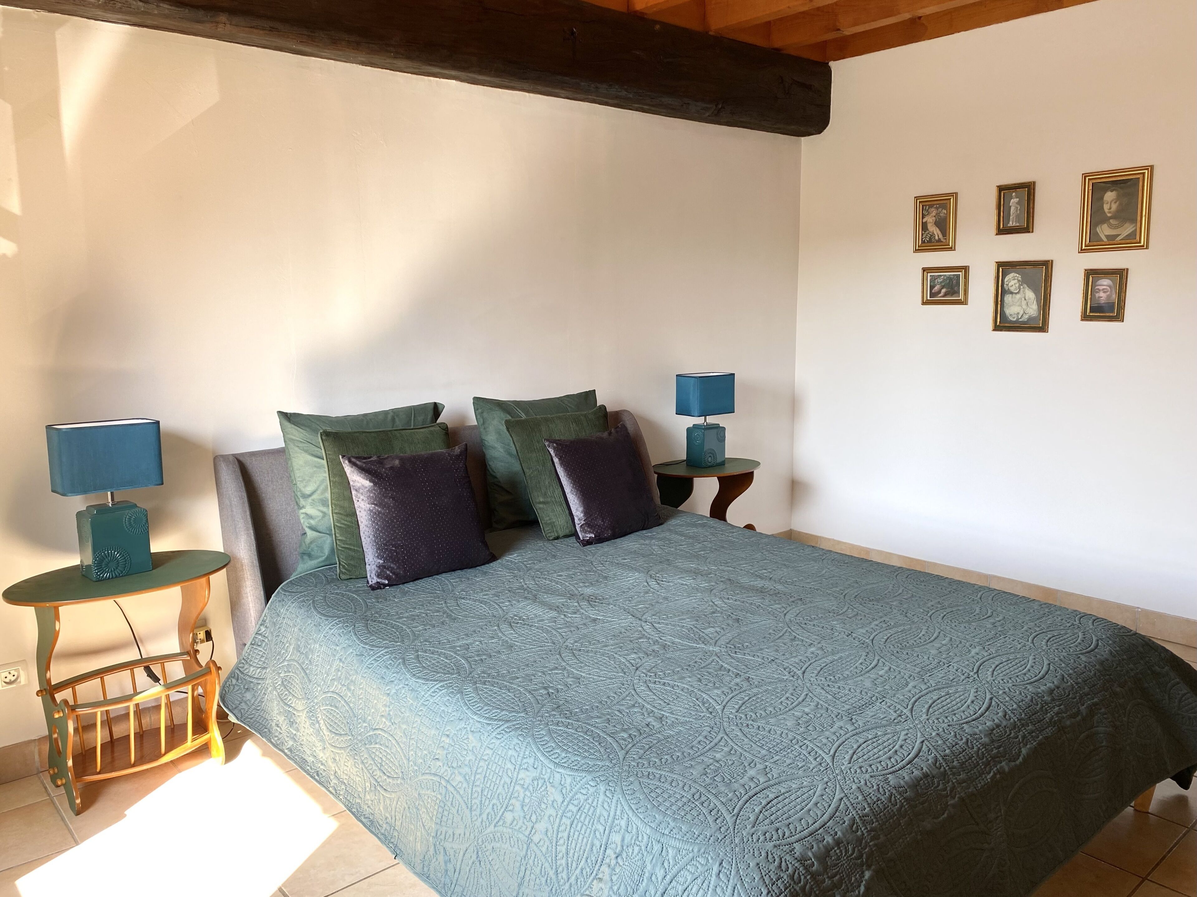 Une chambre à coucher avec un grand lit, deux tables de chevet avec des lampes et un mur orné de tableaux.