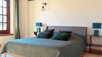 Un dormitorio con techo de madera, una cama con colcha verde, dos mesitas de noche con lámparas y una ventana con cortinas.