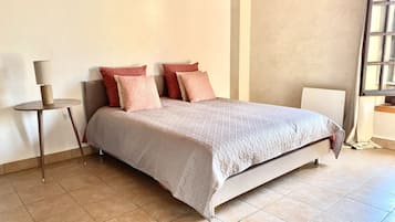 A bedroom with a bed, a bedside table, a lamp, and a window.