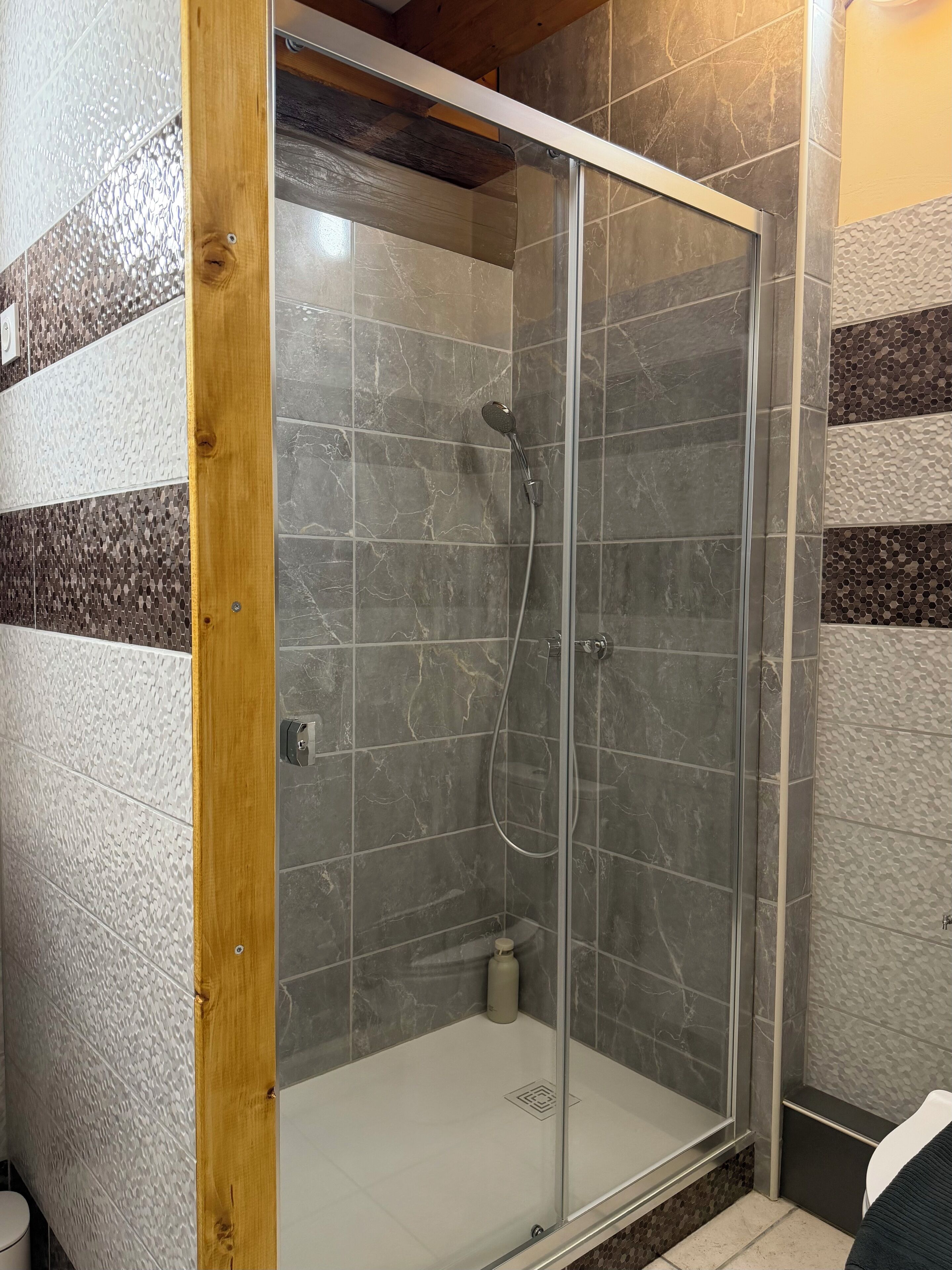 A shower with a glass door, tiled walls, and a wooden frame.
