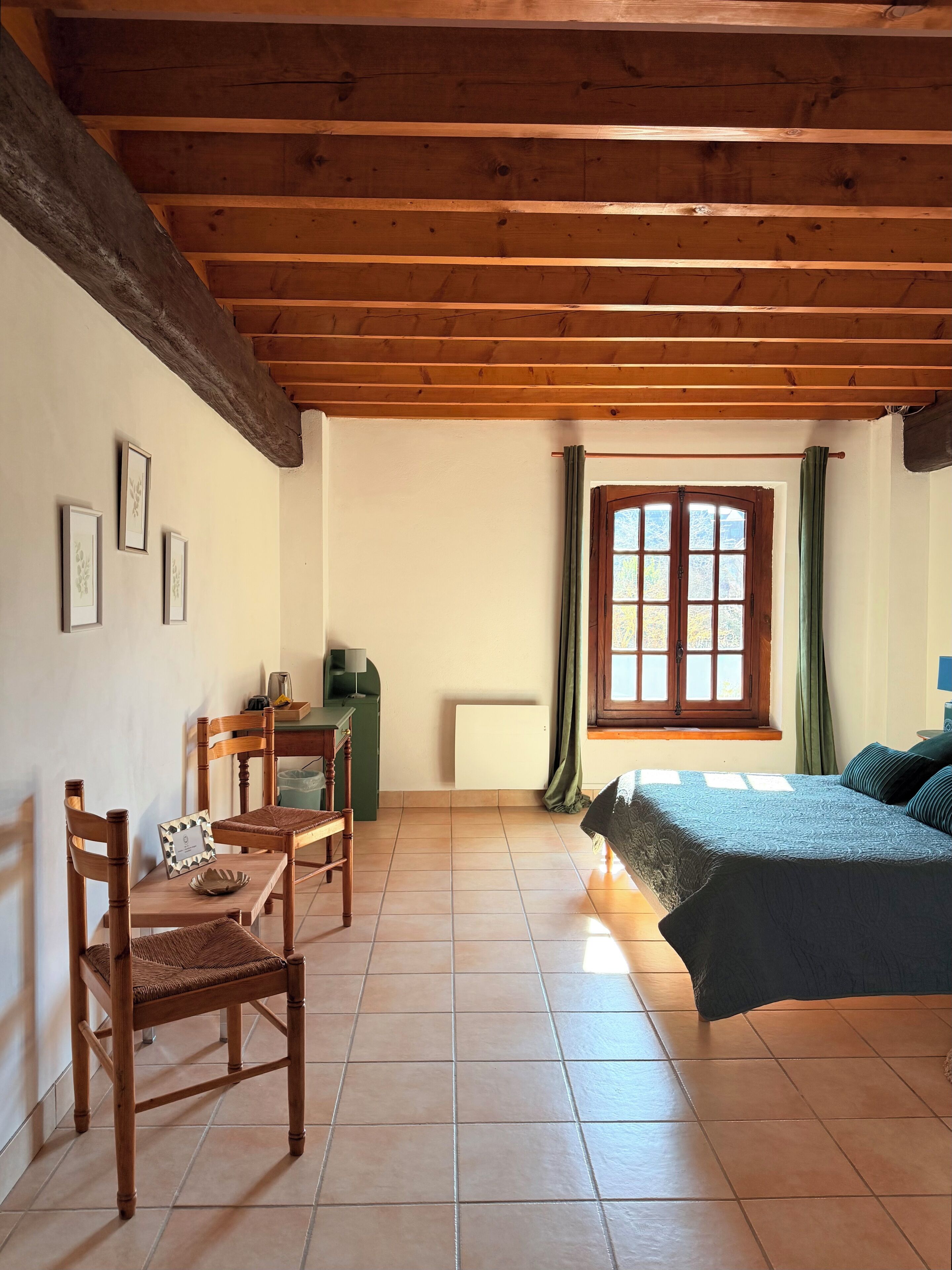 Ein Schlafzimmer mit einem Bett, einem Schreibtisch, Stühlen und einem Fenster mit Vorhängen.