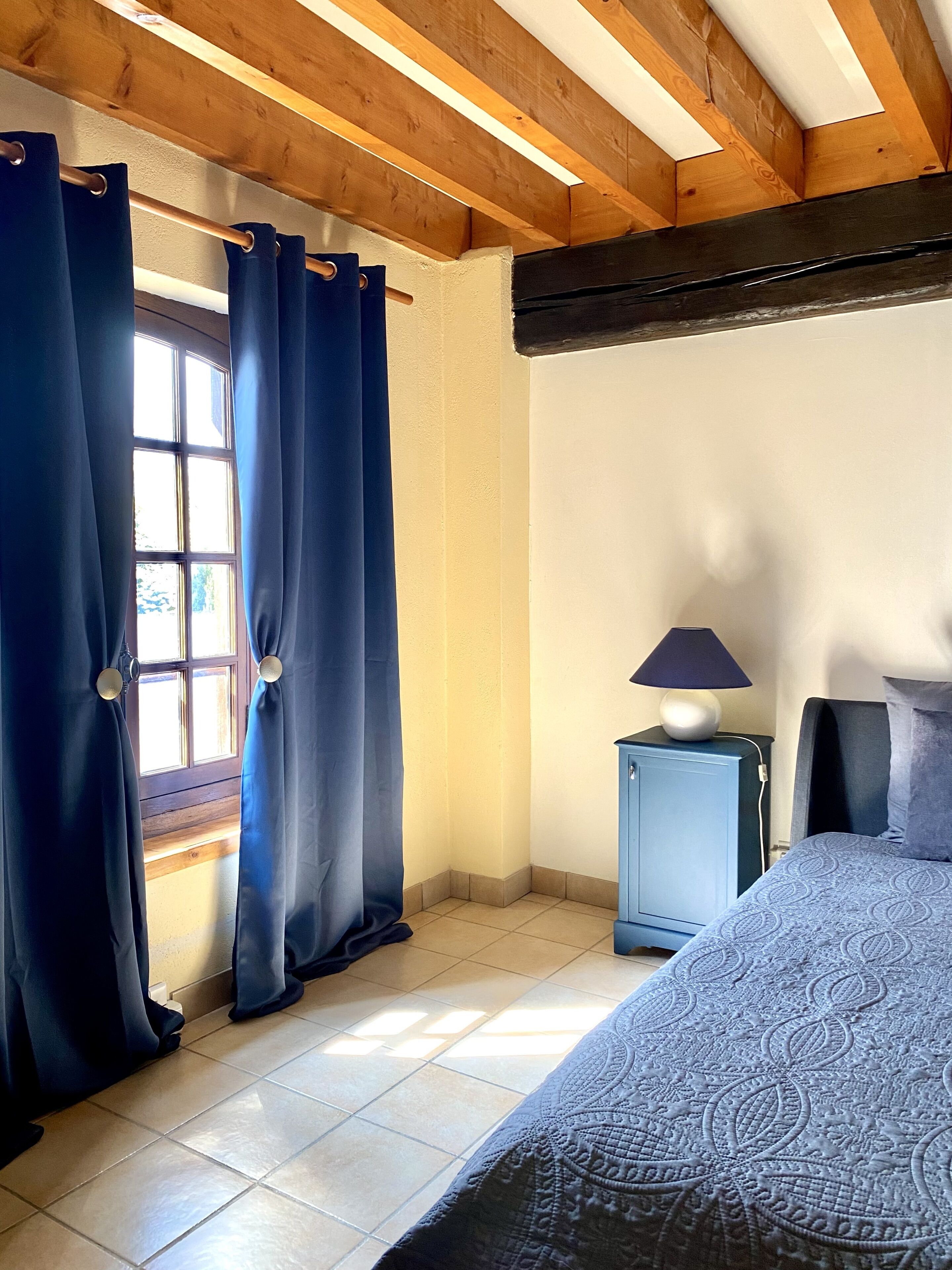 Ein Schlafzimmer mit einem Bett, einem Nachttisch, einer Lampe und einem Fenster mit Vorhängen.