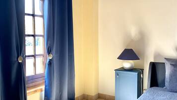 Ein Schlafzimmer mit einem Bett, einem Nachttisch, einer Lampe und einem Fenster mit Vorhängen.