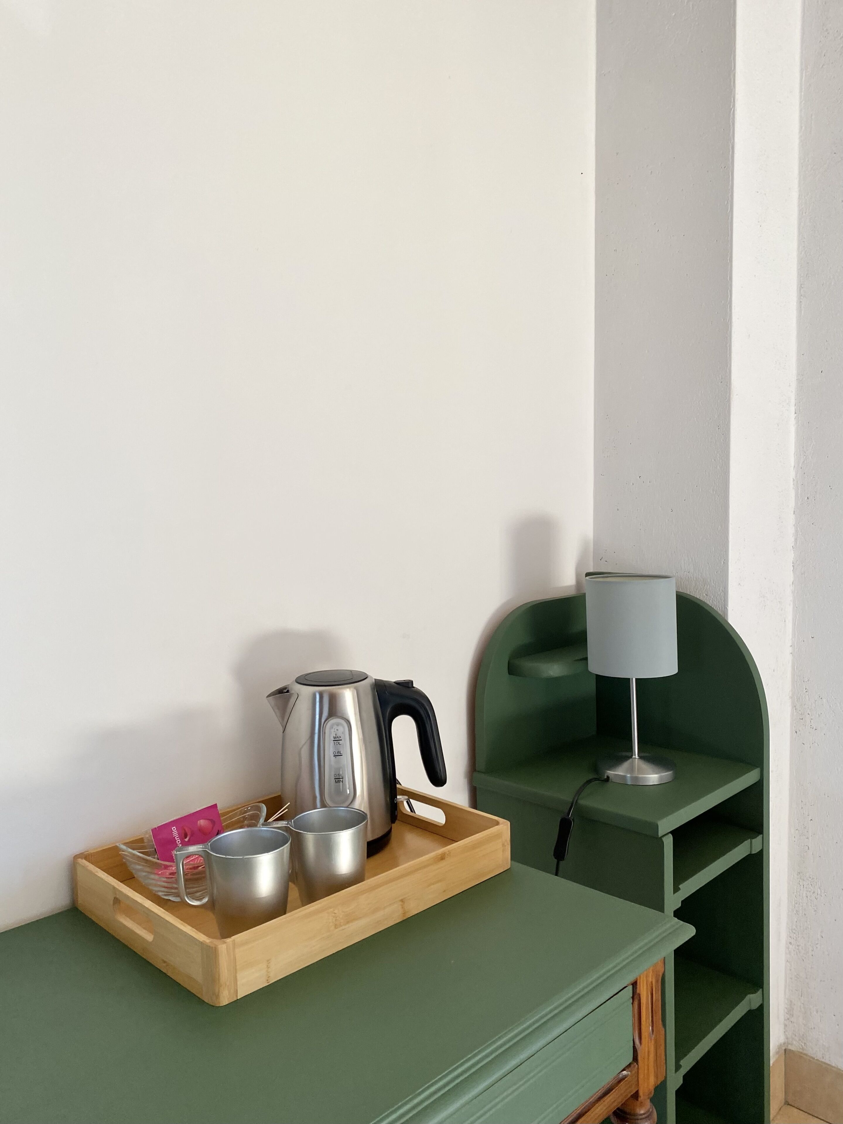 A kitchen area with a wooden tray holding a kettle, a cup, and a small pot. A green chair and a table lamp are also visible.