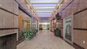 Um hall de hotel moderno com piso de mármore, portas de vidro e uma grande planta em vaso.