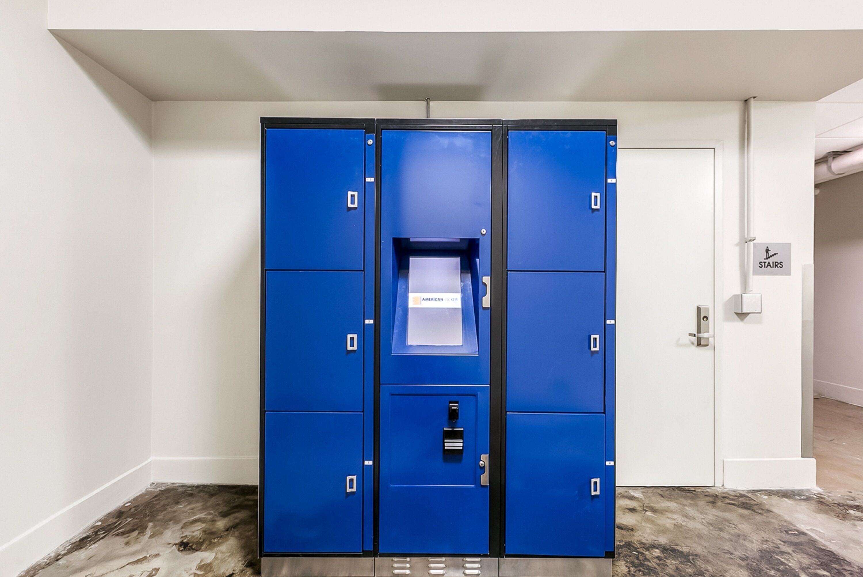 Een blauwe opslagkast met een waterdispenser, in een gang met een witte deur en een bordje dat de trap aangeeft.