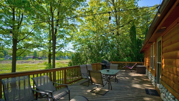 A wooden deck with outdoor furniture, a grill, and a view of a green landscape. - Relaxing Getaway with that UP North Feel! (Beaverton)