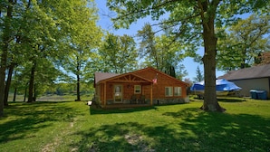 A wooden cabin with a porch, surrounded by trees and a clear sky. - Relaxing Getaway with that UP North Feel! (Beaverton)