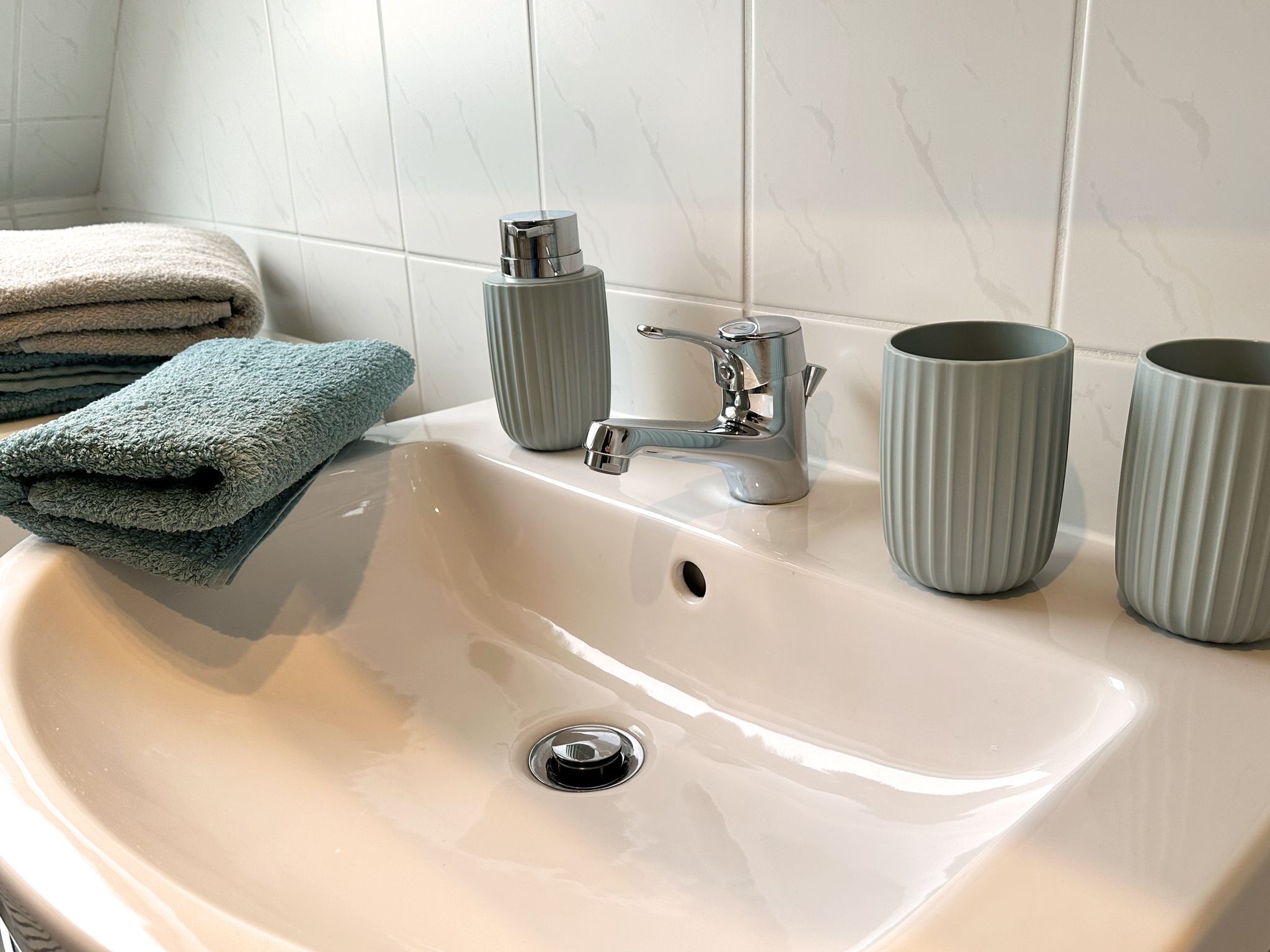 A bathroom sink with a chrome faucet, two ribbed cups, and a stack of folded towels.