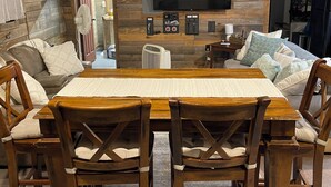 Una mesa de comedor de madera con cuatro sillas, un televisor de pantalla plana montado en la pared y un termostato.