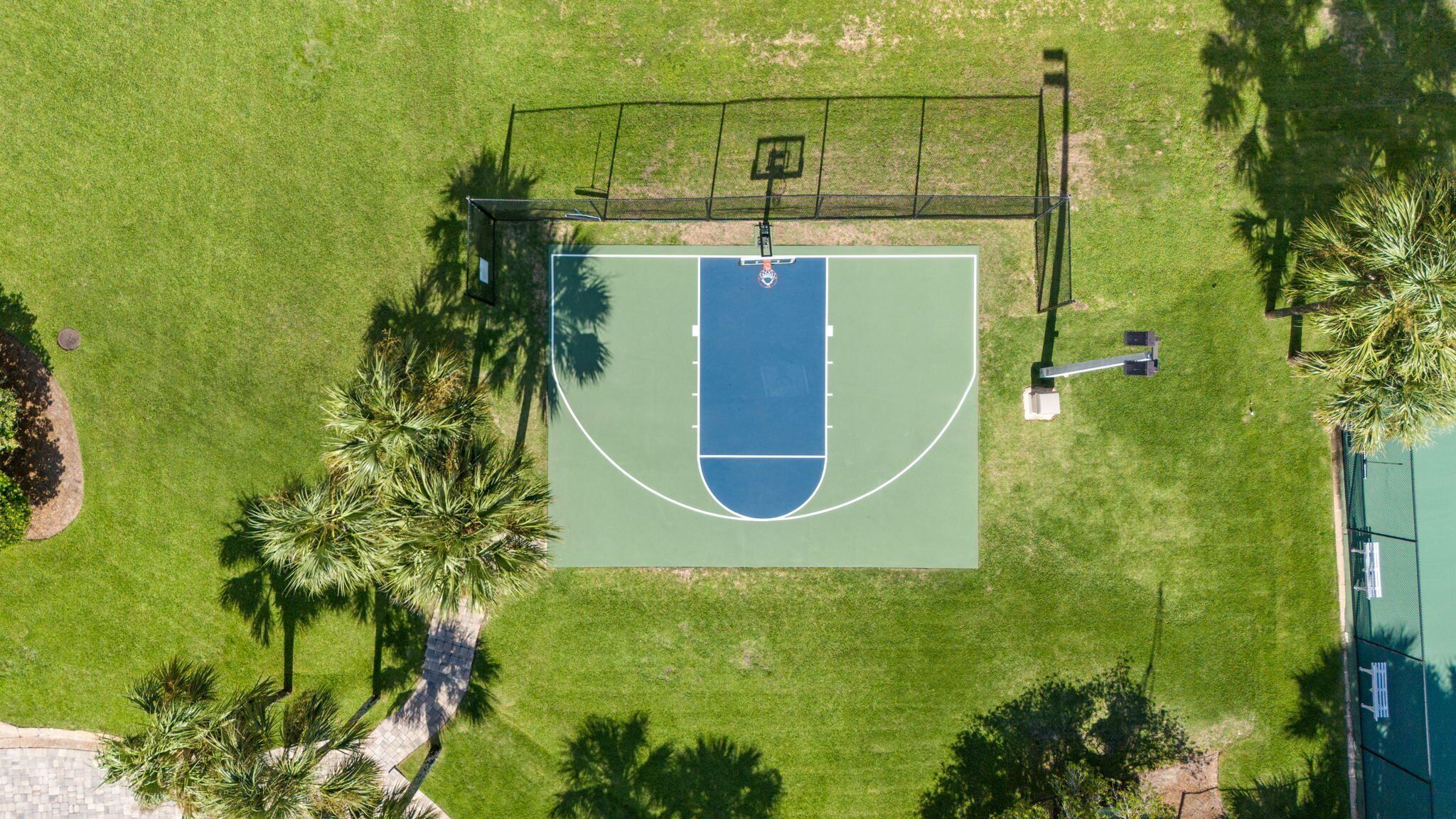 An aerial view of a basketball court surrounded by grass and palm trees.