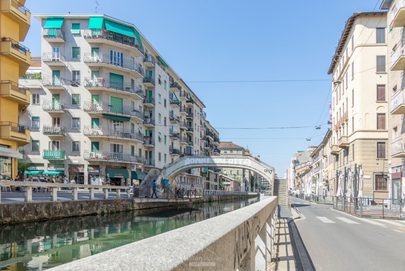 A canal with buildings on either side, a pedestrian bridge, and a clear sky.