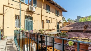 Un bâtiment jaune avec une porte et des fenêtres vertes, un toit recouvert de tuiles et des plantes en pot sur le balcon.