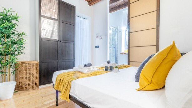 Une chambre d’hôtel avec un lit, un grand miroir, une plante en pot et un plancher en bois.