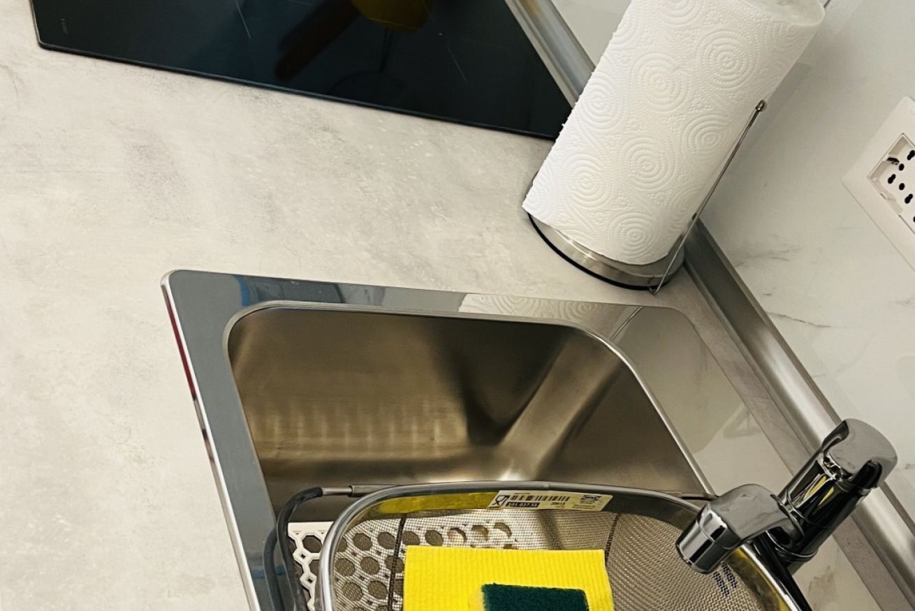 Ein Edelstahlspüle mit einem gelben Schwamm und einer grünen Scheuerschwamm, ein Papierhandtuchhalter und ein Tablet auf der Arbeitsplatte.