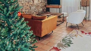 A living room with a stone wall, a Christmas tree, a sofa, a TV, and a chair. - Le Lodge #1 with garden and pool access - Perros Guirec (Perros-Guirec)