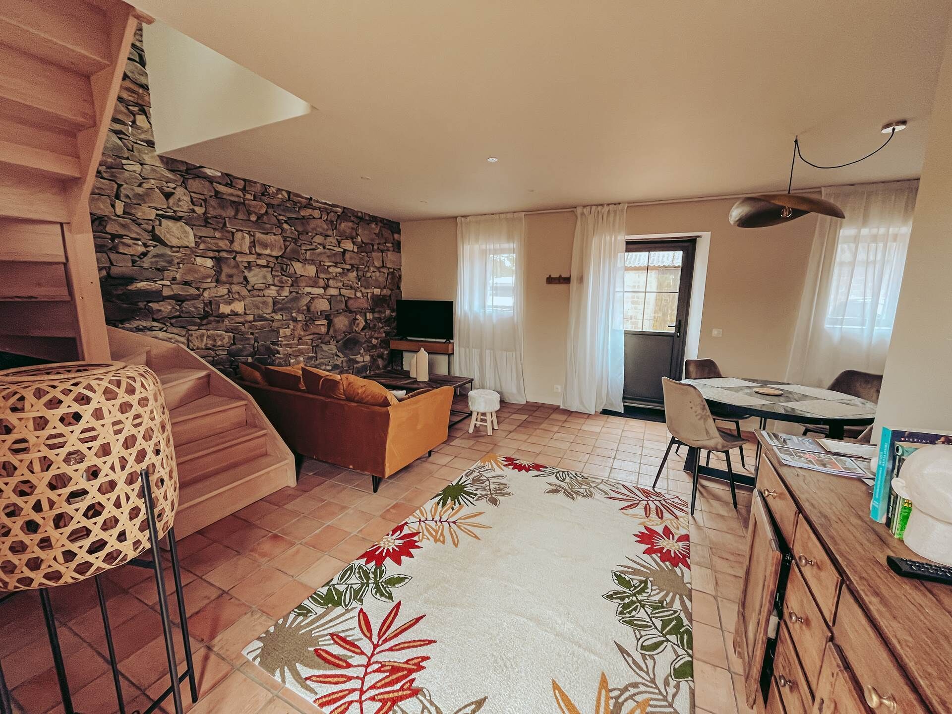 Ein Wohnzimmer mit Steinsäule, einer Couch, einem Couchtisch, einem Esstisch mit Stühlen und einer Treppe.