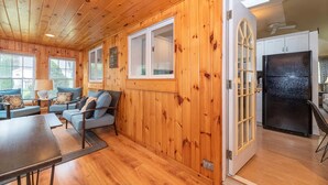 Interior acogedor de una cabaña con paredes de madera, una zona de comedor y una cocina con refrigerador.
