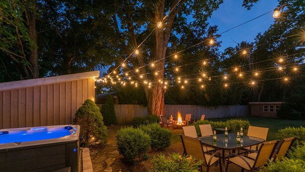 Un patio trasero con jacuzzi, mobiliario exterior e iluminación colgante.