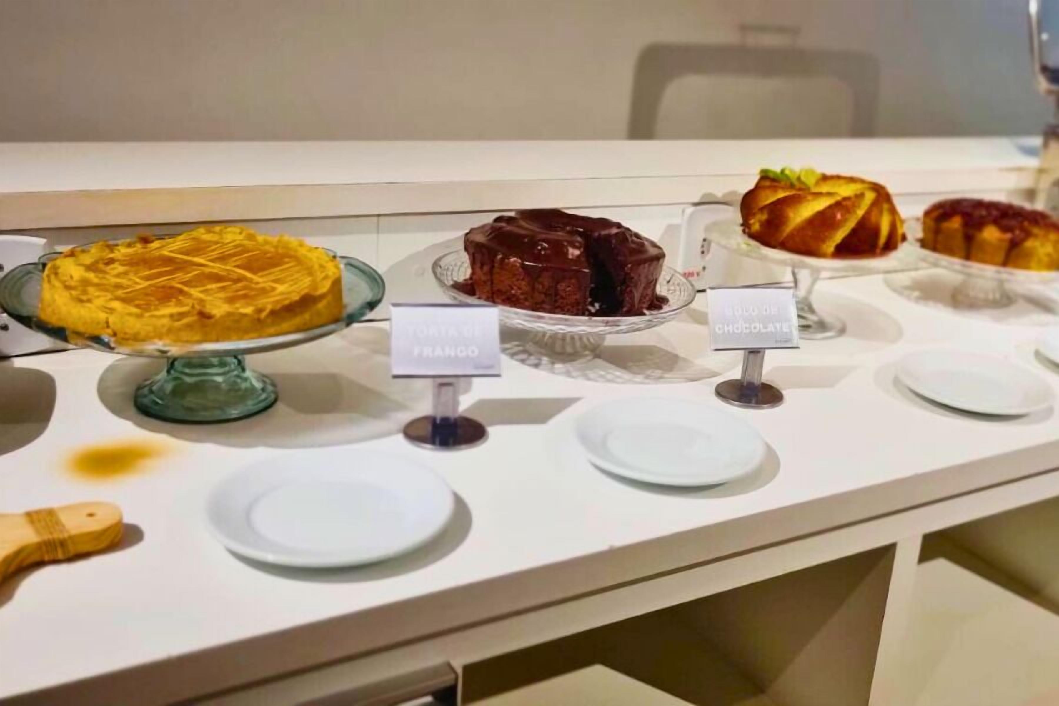 En dessertbuffé med olika sorters tårtor och bakverk presenterade på glasfat, där varje bakverk är försett med en etikett som anger dess namn.