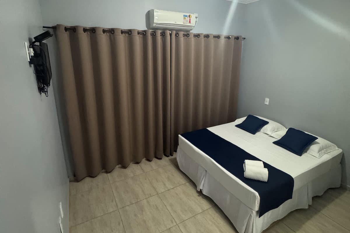 Ein Schlafzimmer mit Bett, Vorhängen, einer Klimaanlage und einer Deckenleuchte.
