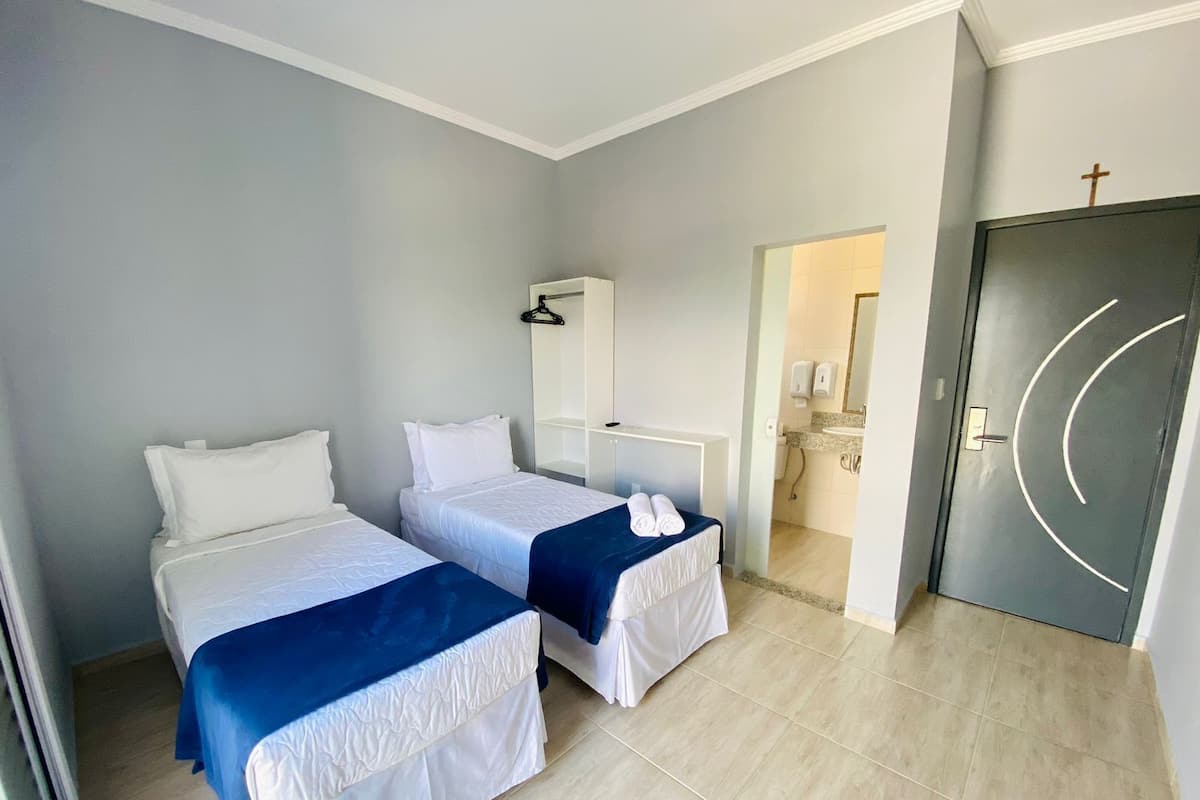 Ein Hotelzimmer mit zwei Betten, einem Badezimmer und einer Tür mit einem Kreuz.