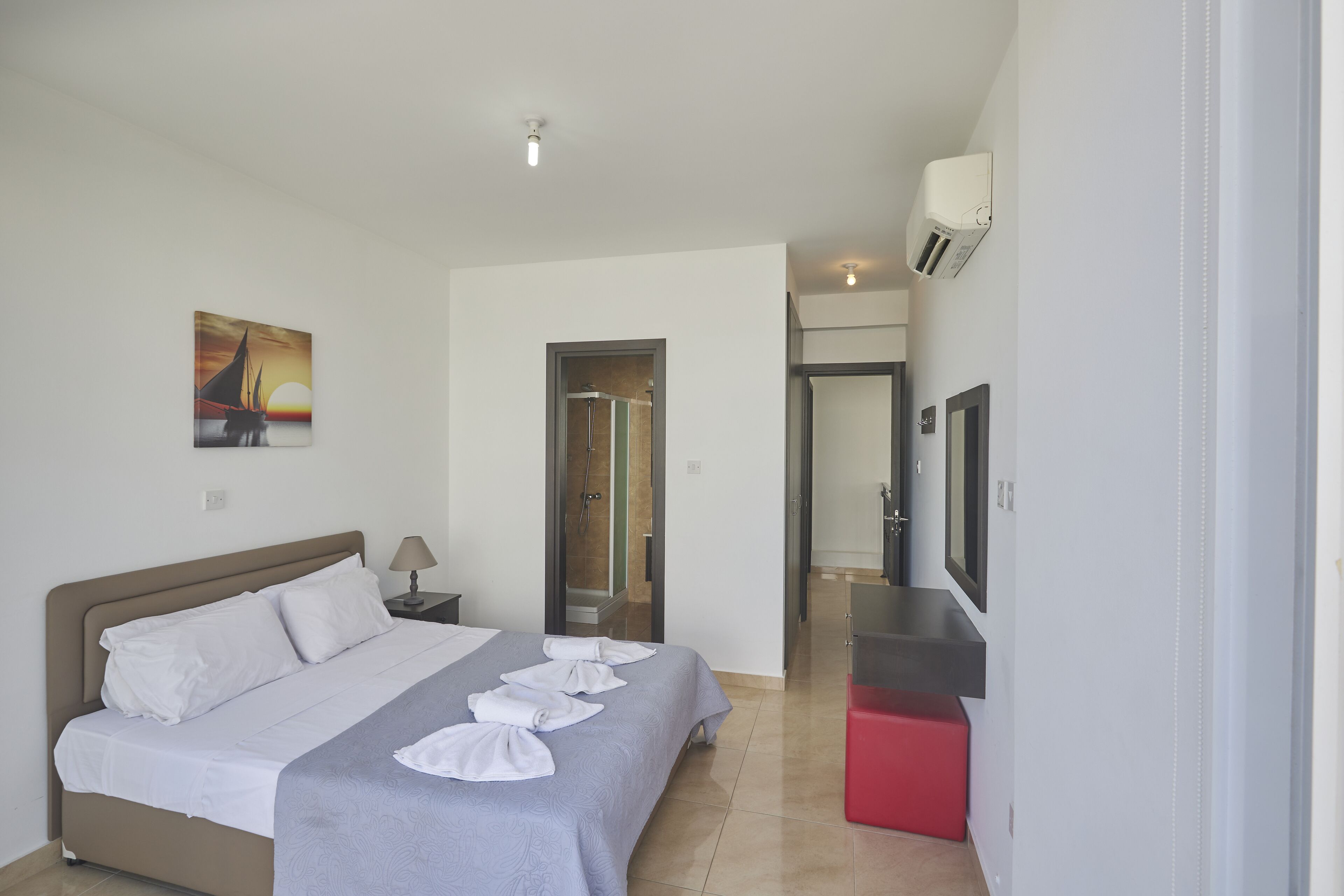 A hotel room with a bed, a TV, a shower, and a hallway leading to another room.