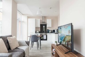 A modern living room with a grey sofa, a wooden coffee table, and a flat-screen TV mounted on the wall.