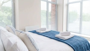 A hotel room with a large bed, a blue blanket, and white towels. - Manchester & Salford | 1BED Apartment with Parking (Salford)