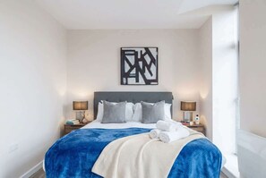 A neatly made bed with a blue and white blanket, two bedside lamps, and a modern abstract art piece on the wall.