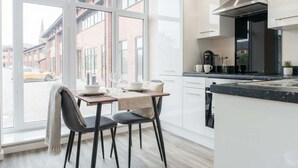 A modern kitchen with white cabinets, a black countertop, and a large window overlooking a street. - Manchester & Salford | 1BED Apartment with Parking (Salford)
